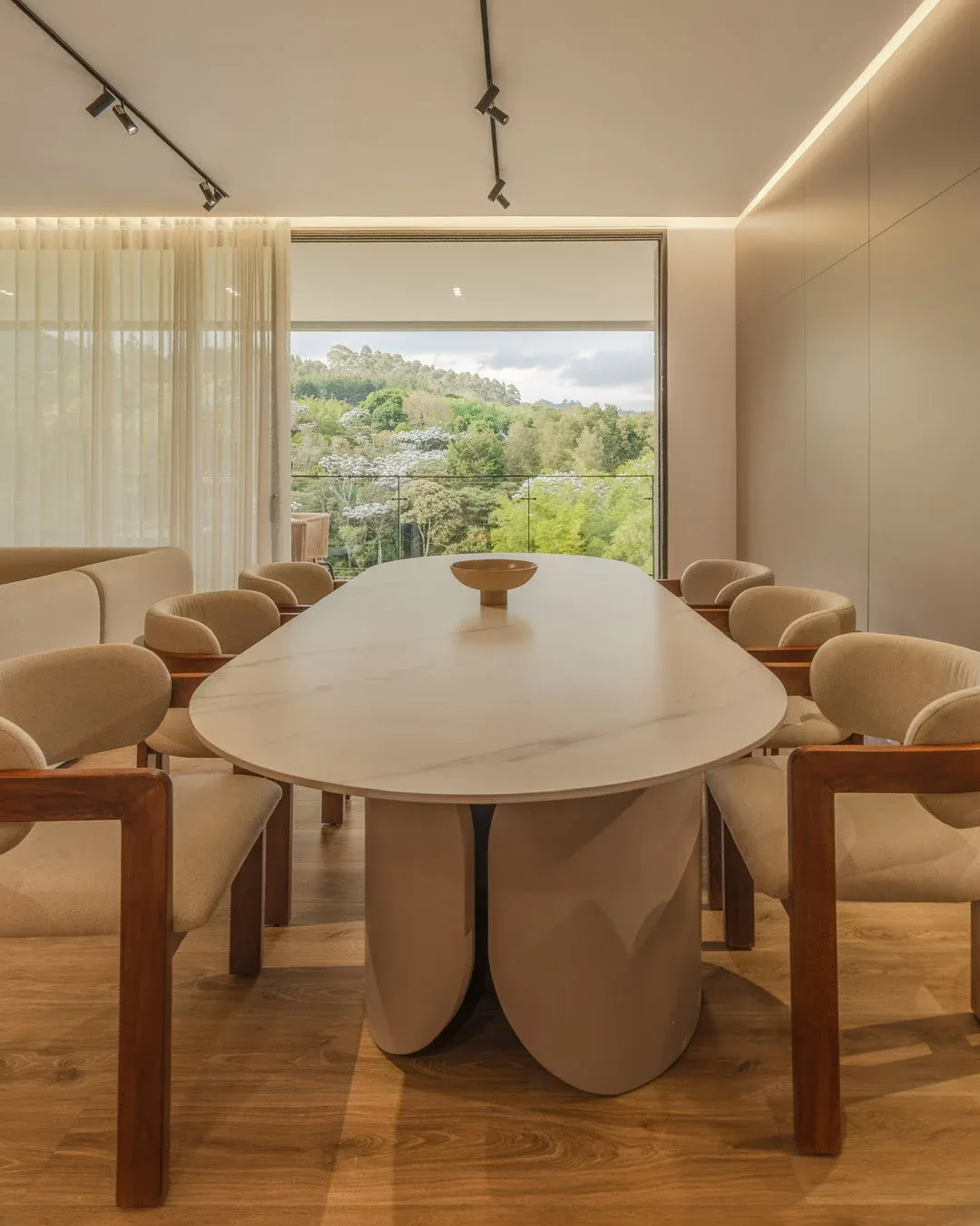 Un comedor formal con una gran mesa ovalada de superficie clara y varias sillas de madera tapizadas