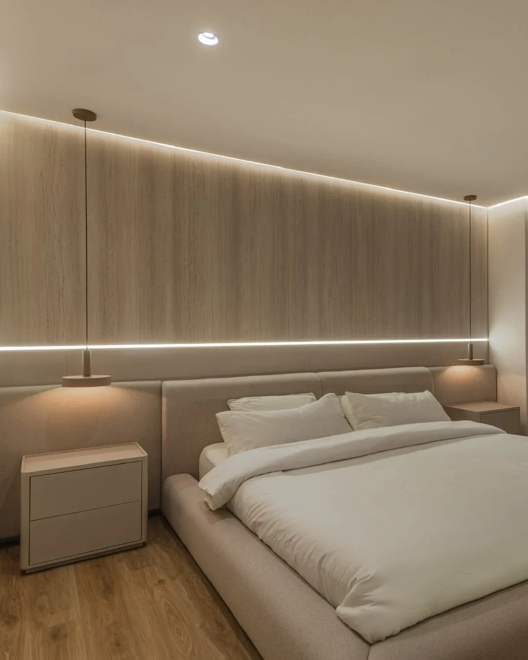 Vista general de un dormitorio principal, destacando una cama grande con cabecero tapizado claro