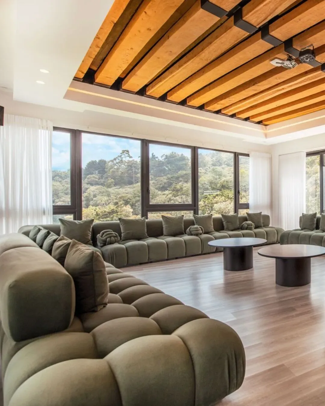 Sala principal con sofá modular acolchado, tonos naturales y grandes ventanales.