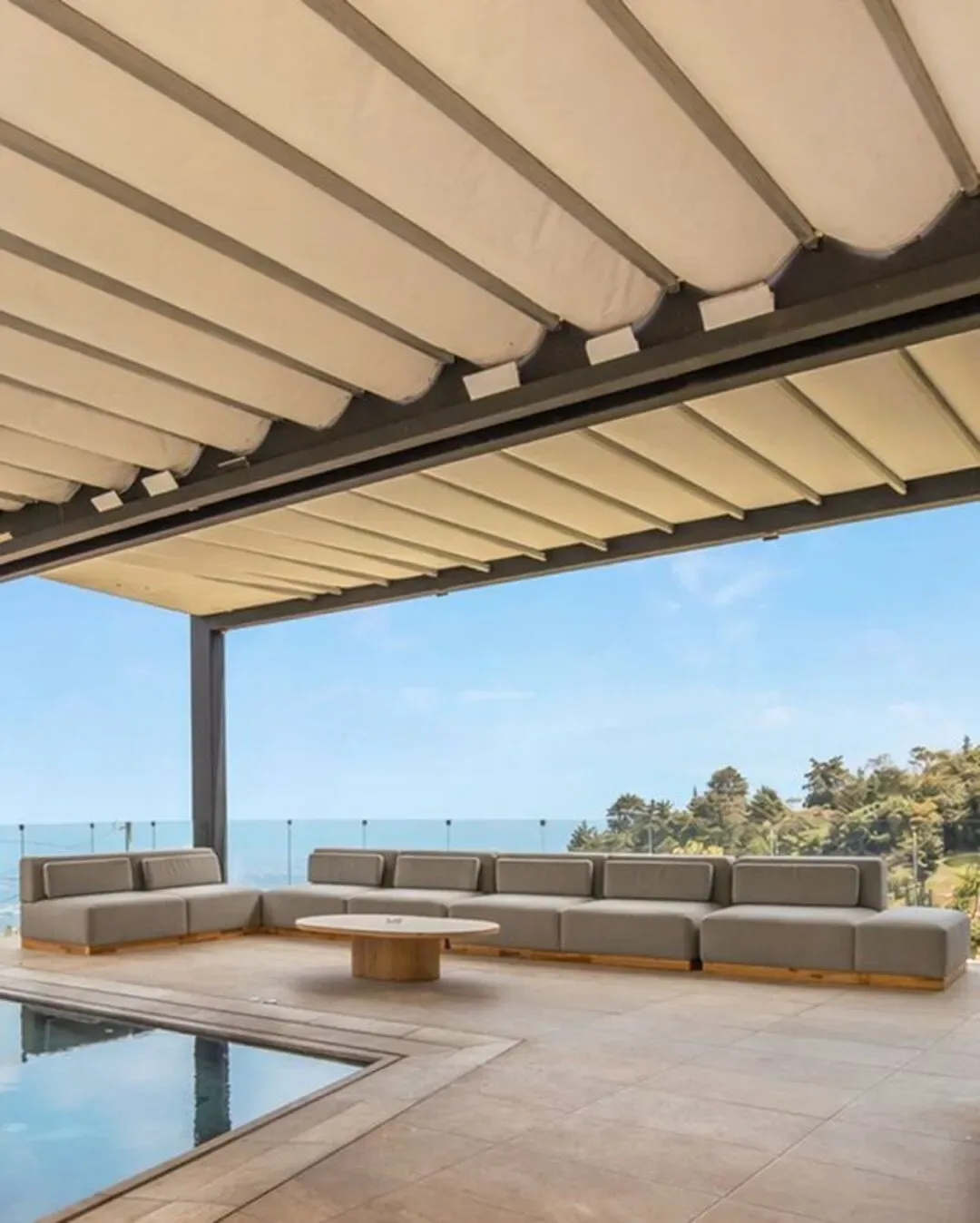 Zona de piscina con sofá exterior modular, sombra arquitectónica y vistas abiertas.