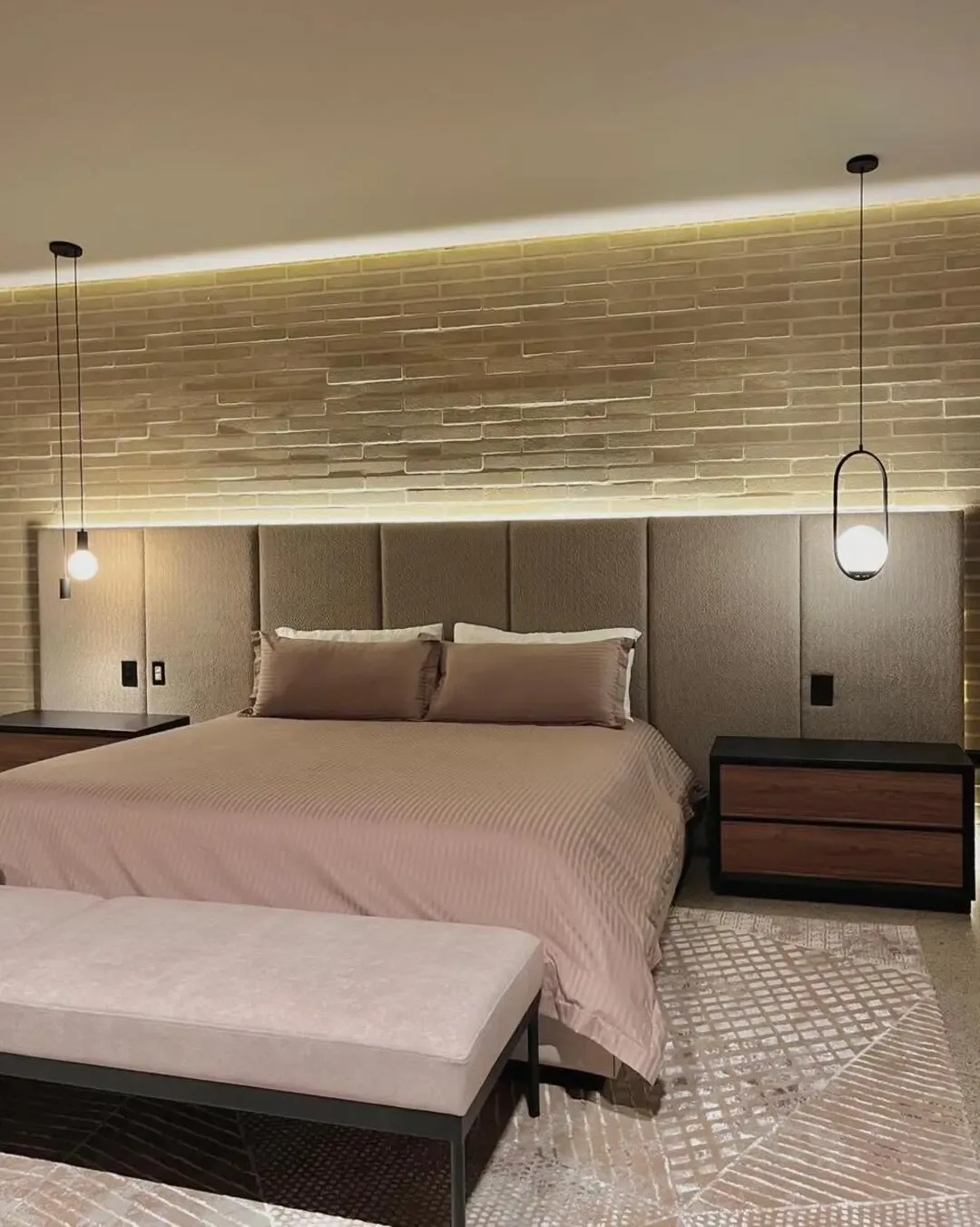 Dormitorio cálido con cabecero tapizado, ladrillo rústico, madera y detalles de alto confort.