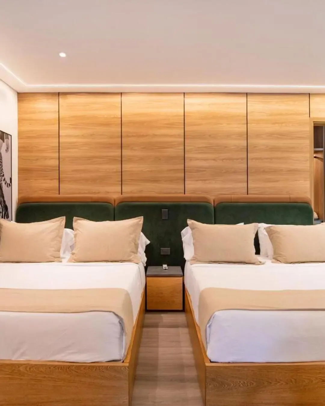 Dormitorio hotelero con camas dobles, tapizados verdes, madera cálida y composición simétrica.