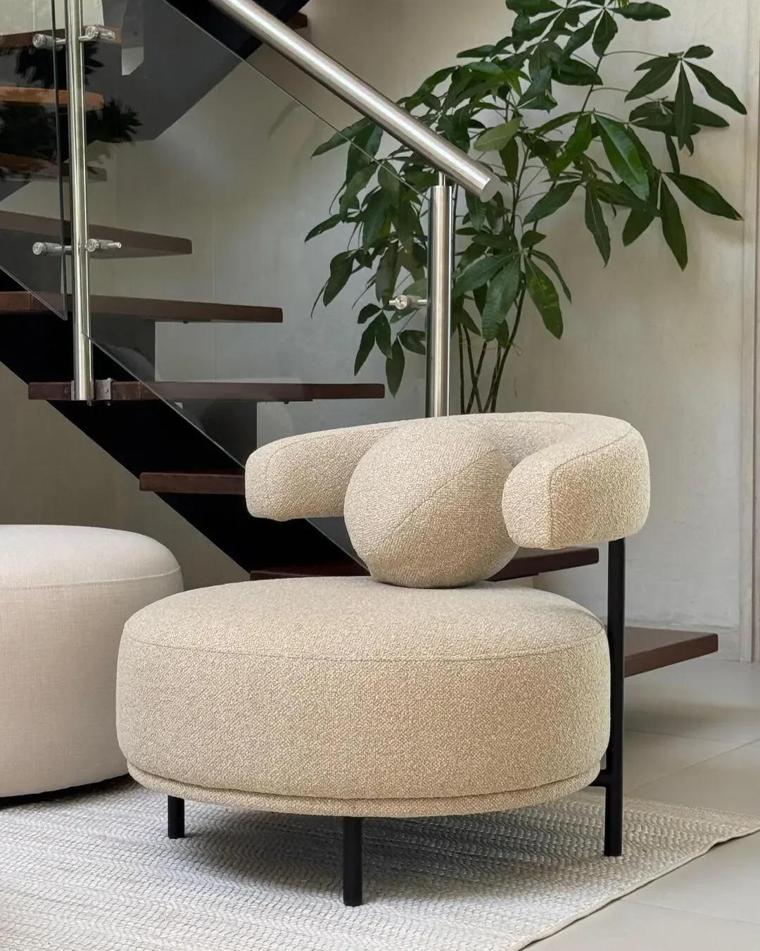 Organic bouclé upholstered chair with black frame, staircase, and indoor greenery.
