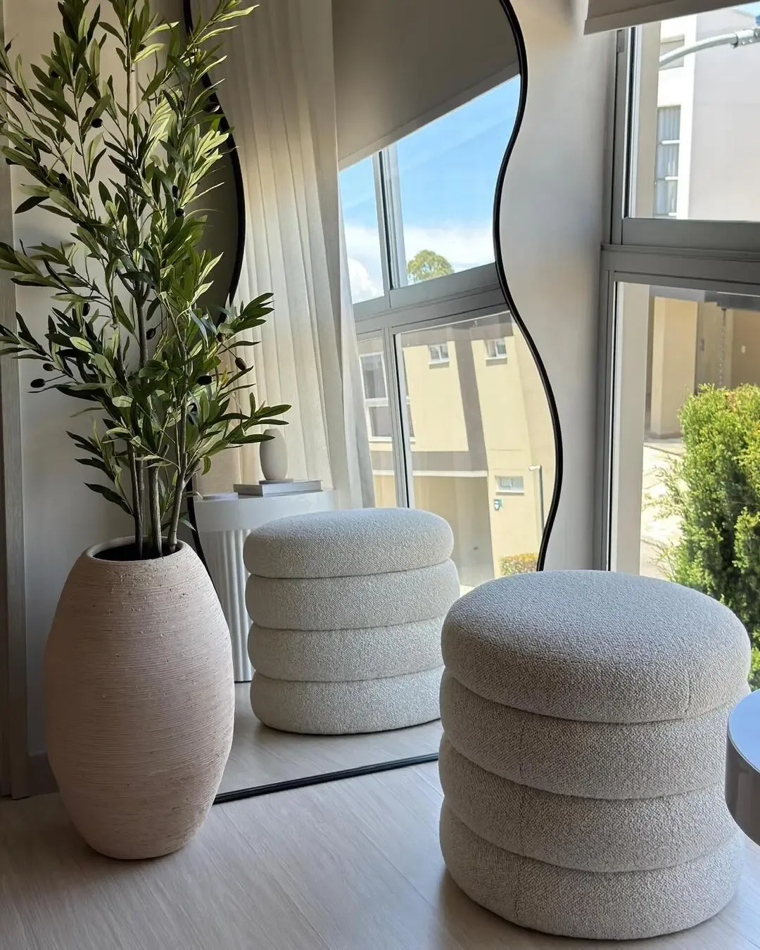 Bright corner with organic mirror, textured pouf, and decorative greenery.