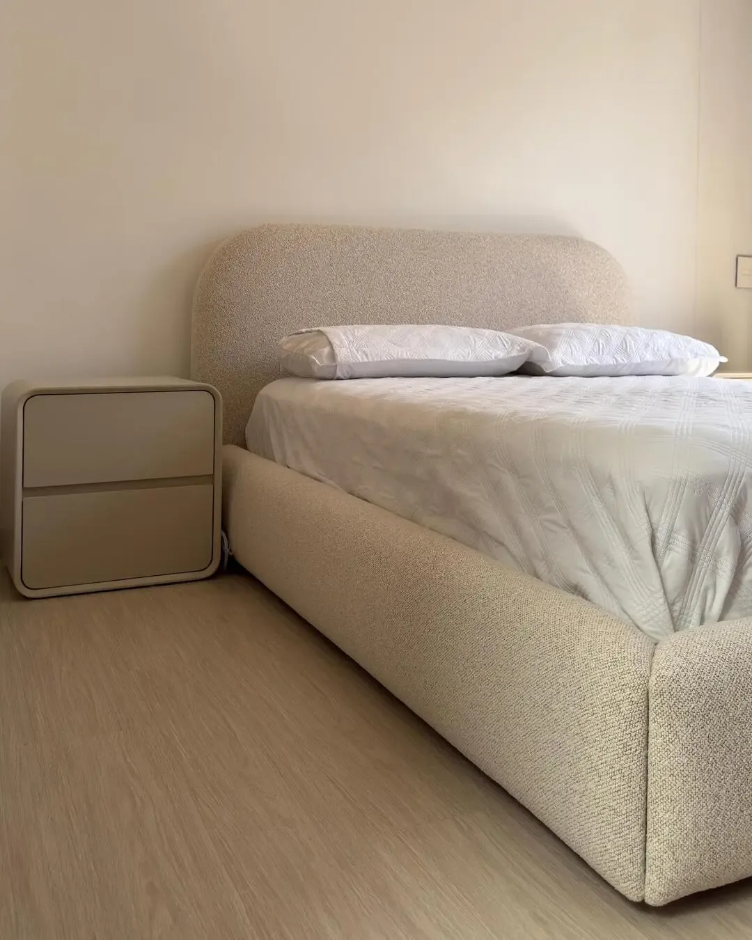 Warm bedroom with upholstered bed, rounded shapes, and neutral-toned furniture.