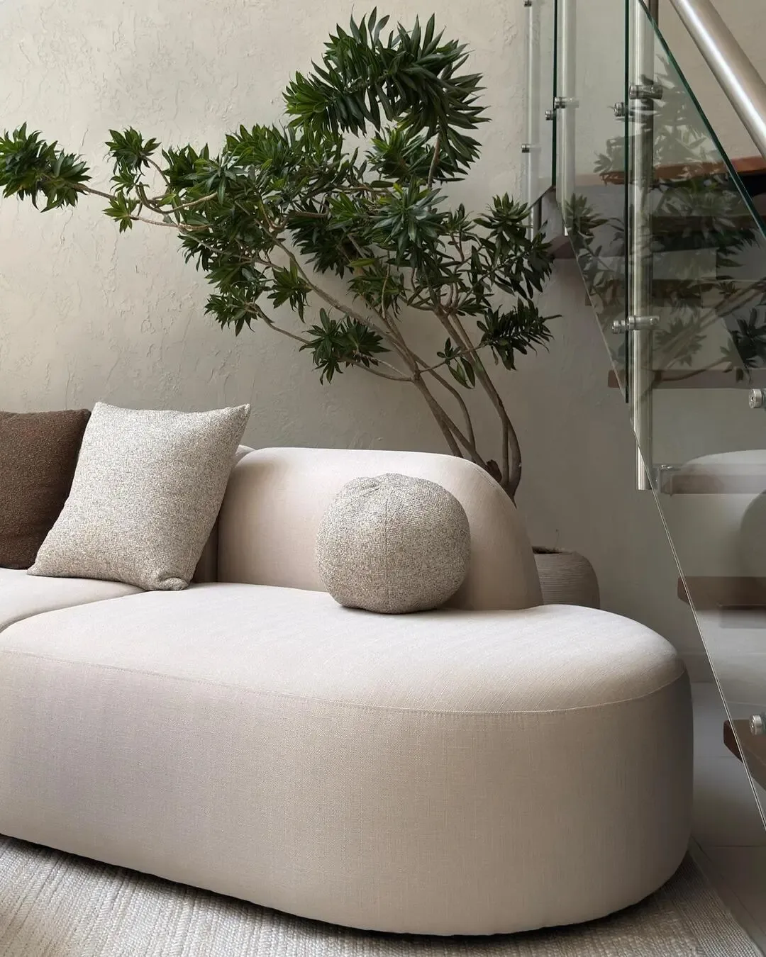 Curved sofa beside indoor greenery, modern staircase, and soft textures.