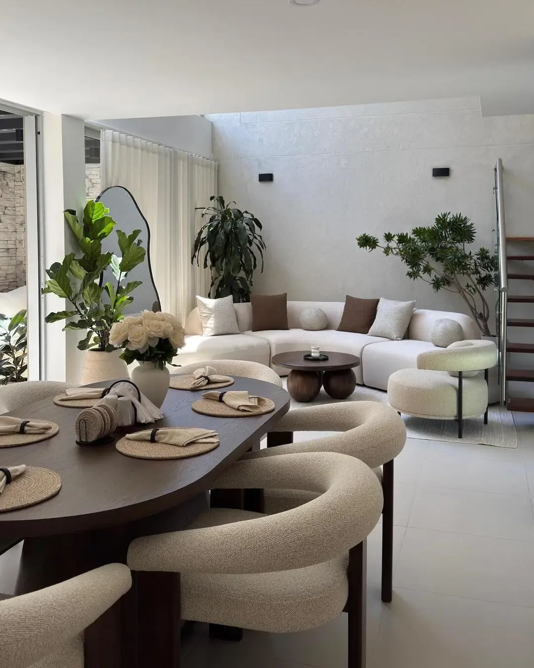 Integrated dining and living area with organic shapes, dark wood, and natural greenery.