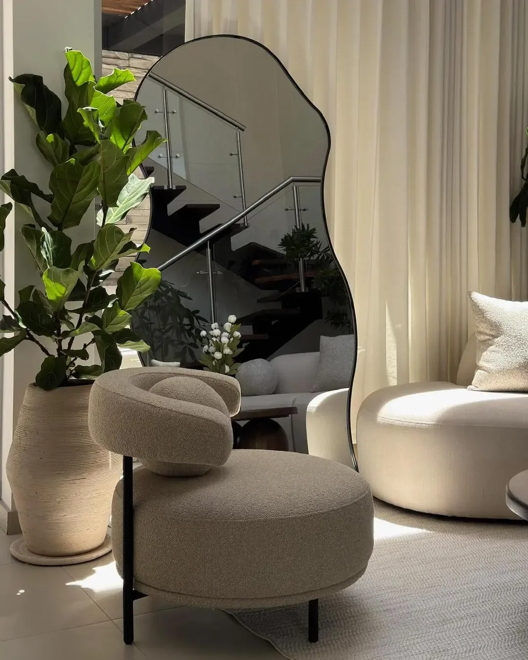 Sophisticated corner with organic mirror, greenery, upholstered chair, and natural light.