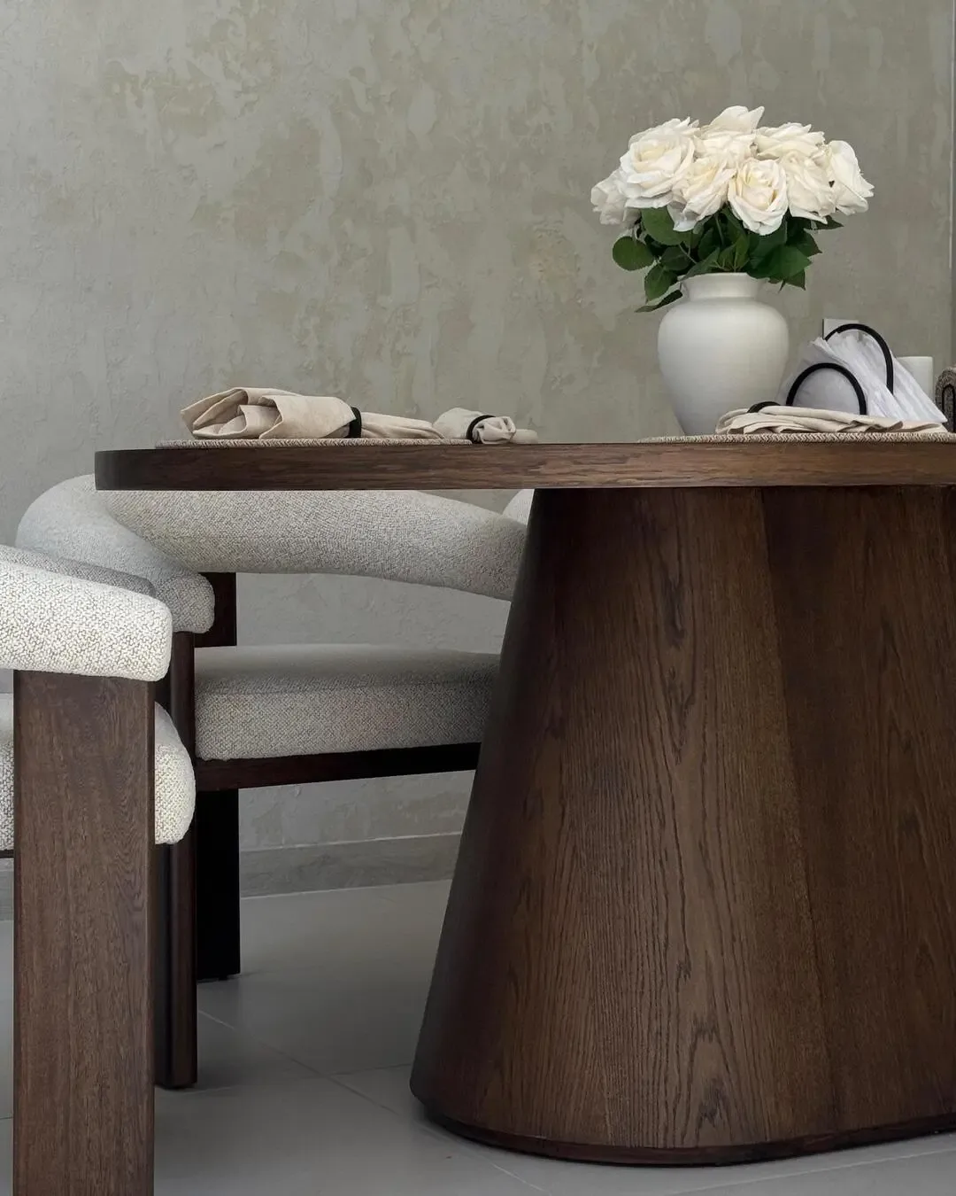 Dining detail with sculptural wooden table and enveloping upholstered chairs.