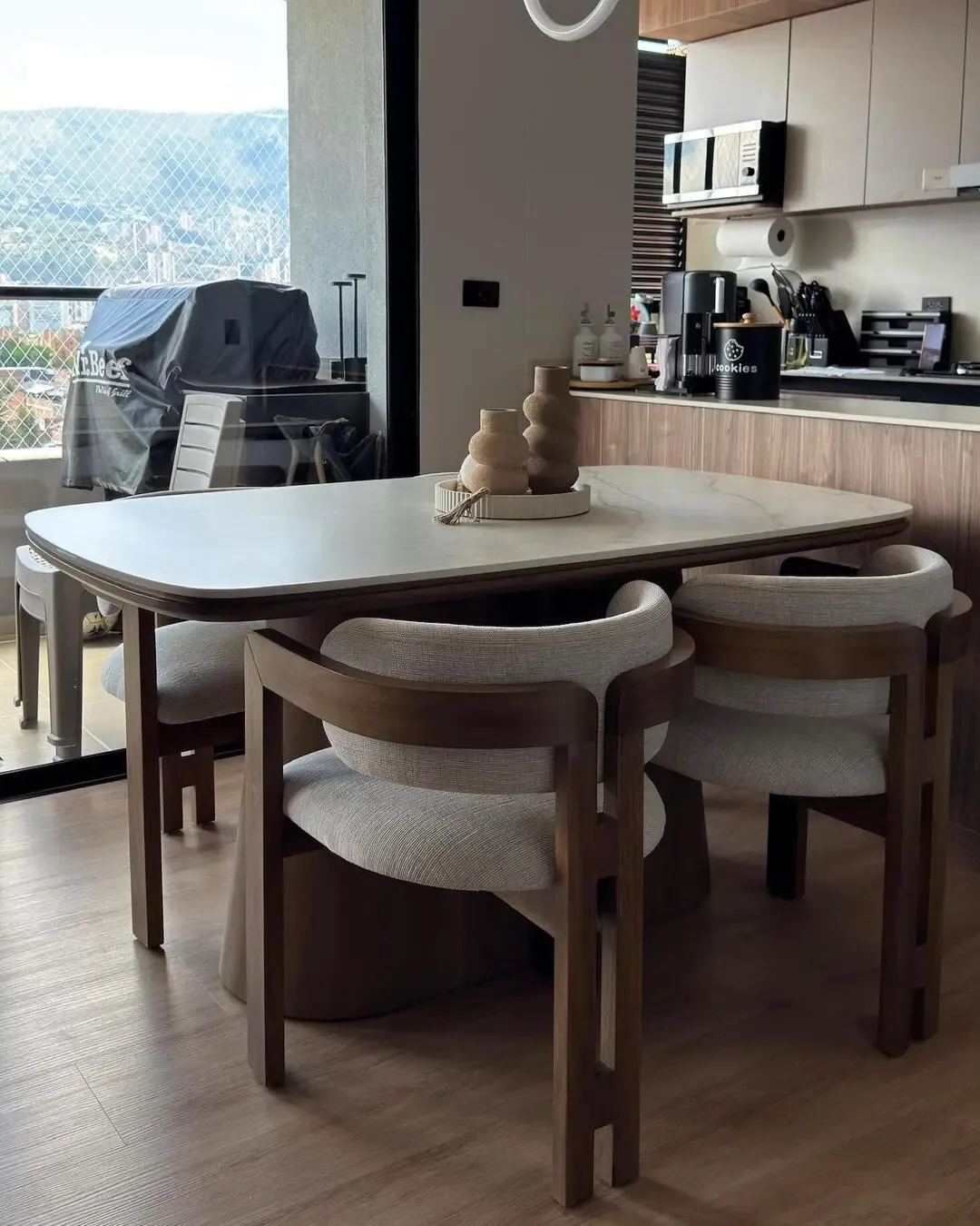 Comedor junto a la cocina con sillas ergonómicas, madera natural y vista exterior.