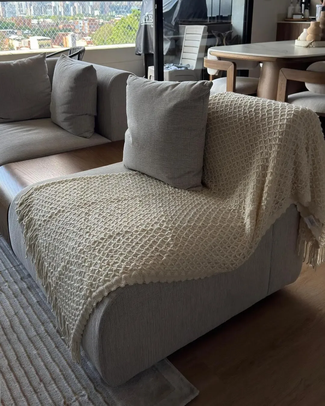 Chaise tapizado con manta tejida, cojines neutros y una atmósfera acogedora.