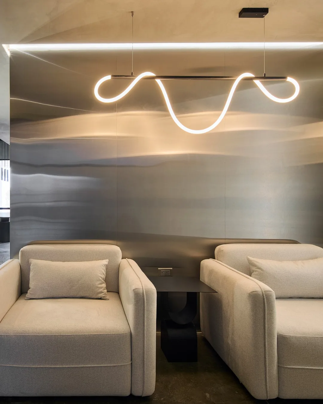 Sala de espera moderna con sillones tapizados beige, mesa lateral negra y lámpara LED escultural sob