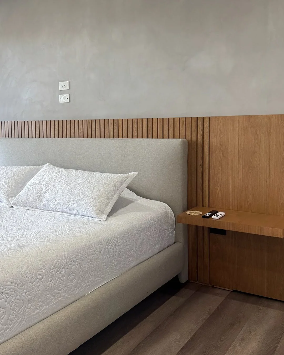 Vista lateral de una cama moderna con cabecero alto y ropa de cama con texturas bordadas.