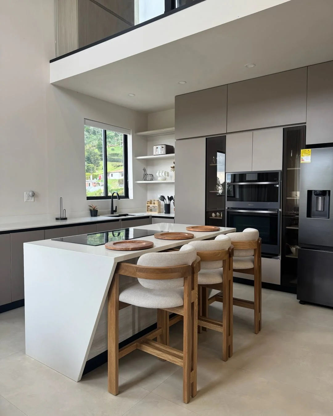 Cocina moderna con isla central blanca y tres sillas altas de madera con diseño curvo.