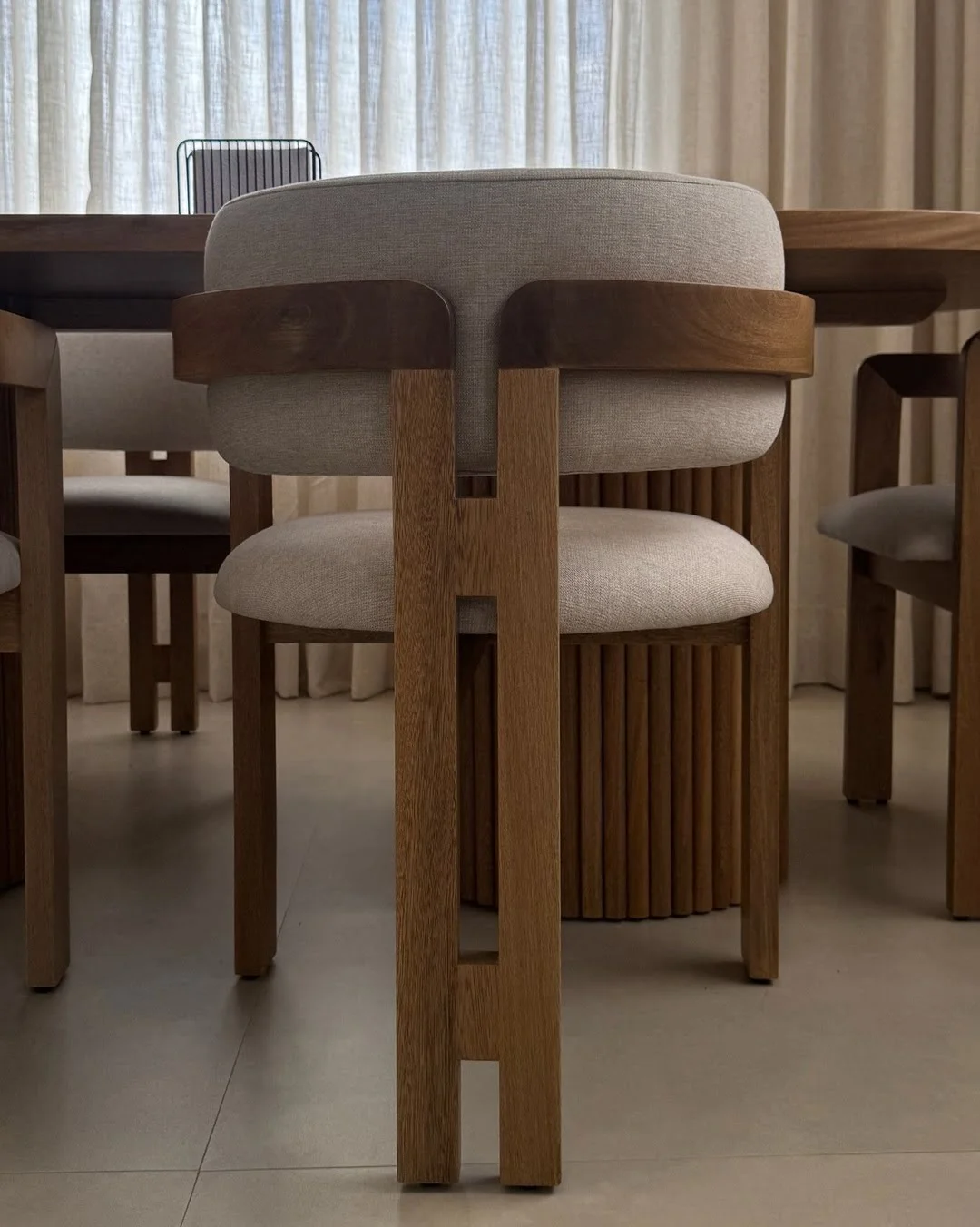 Detalle del respaldo curvo de una silla de comedor en madera natural con tapizado claro.