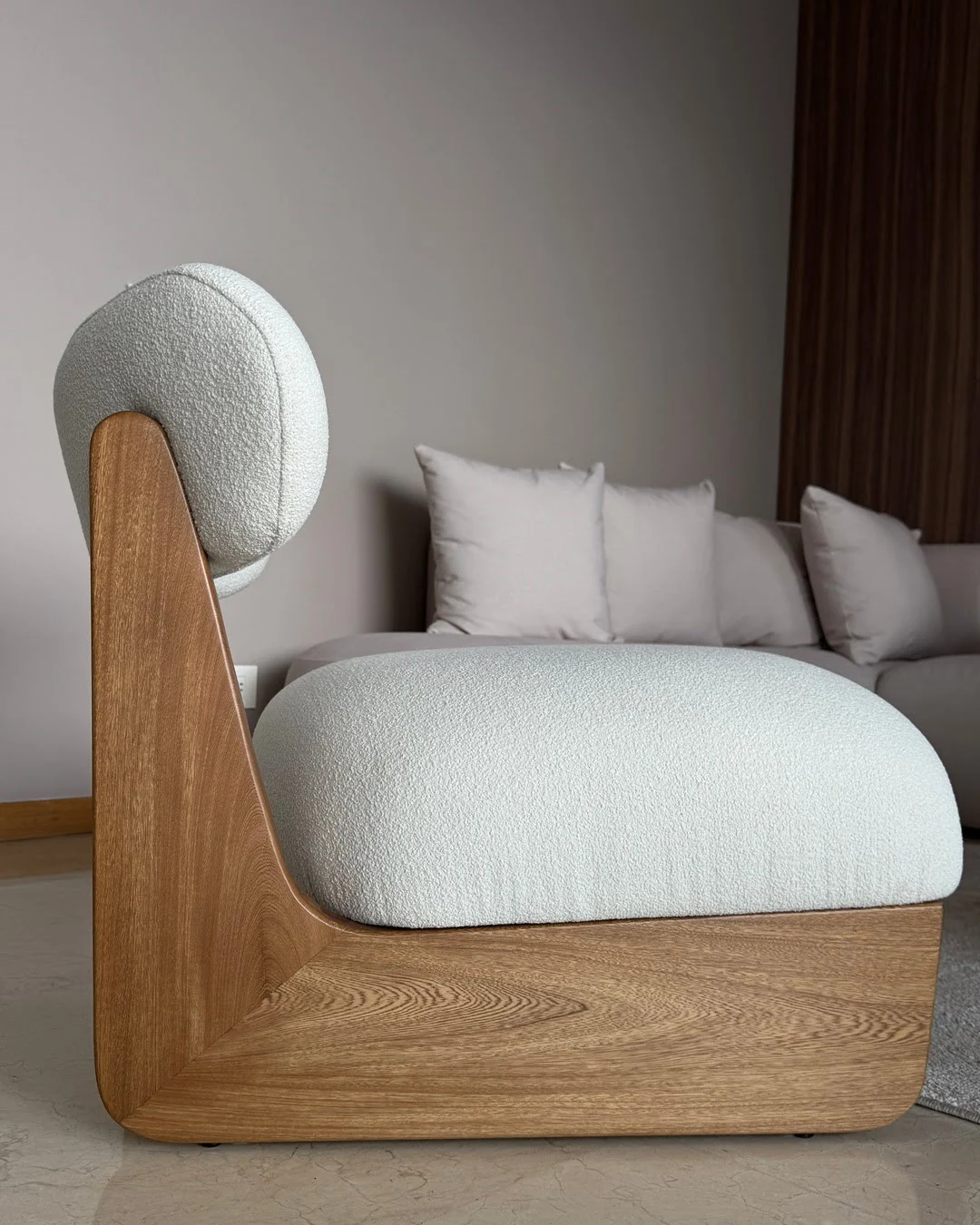 Perfil de una poltrona de diseño con base de madera maciza y tapizado blanco texturizado.