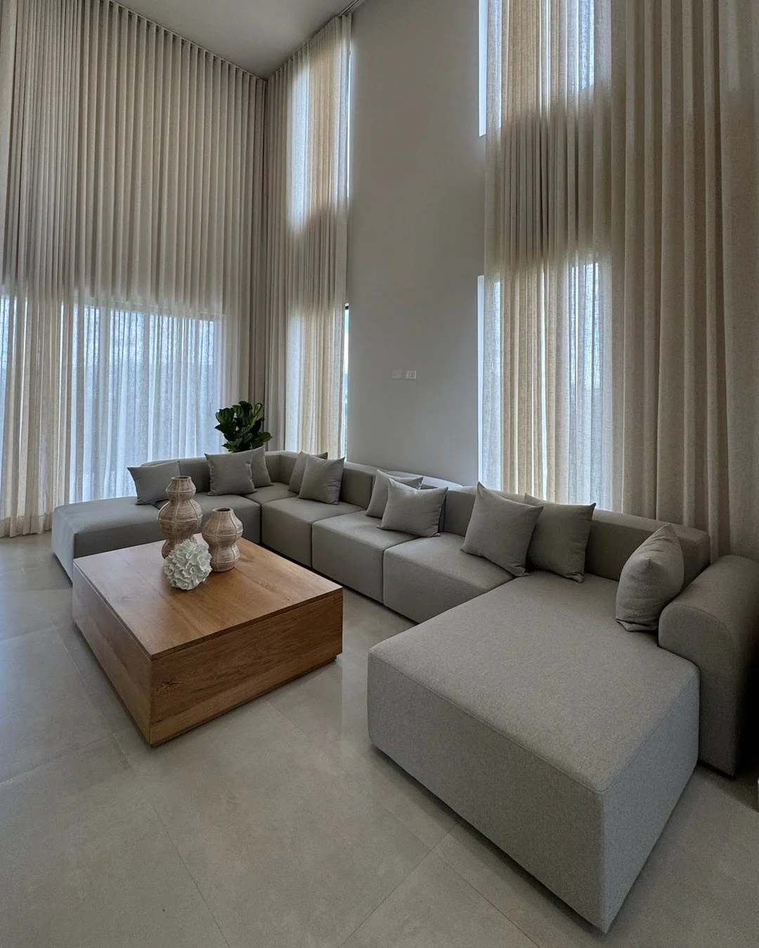 Composición de sala de estar con sofá en L de gran formato, techos altos y cortinas de gran caída.