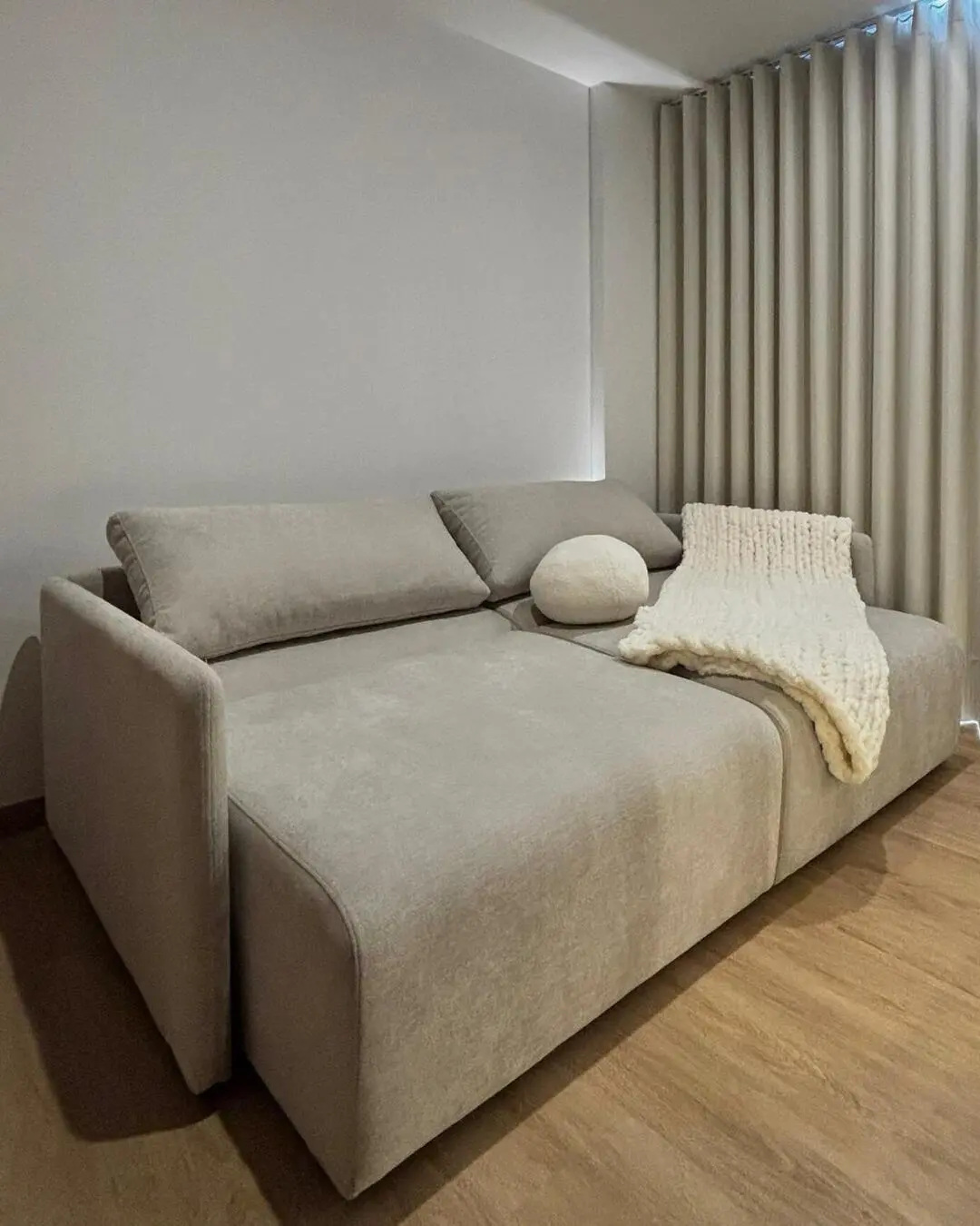 Sofá cama moderno en tonos grises neutros con cojines decorativos y una manta, en un ambiente minima