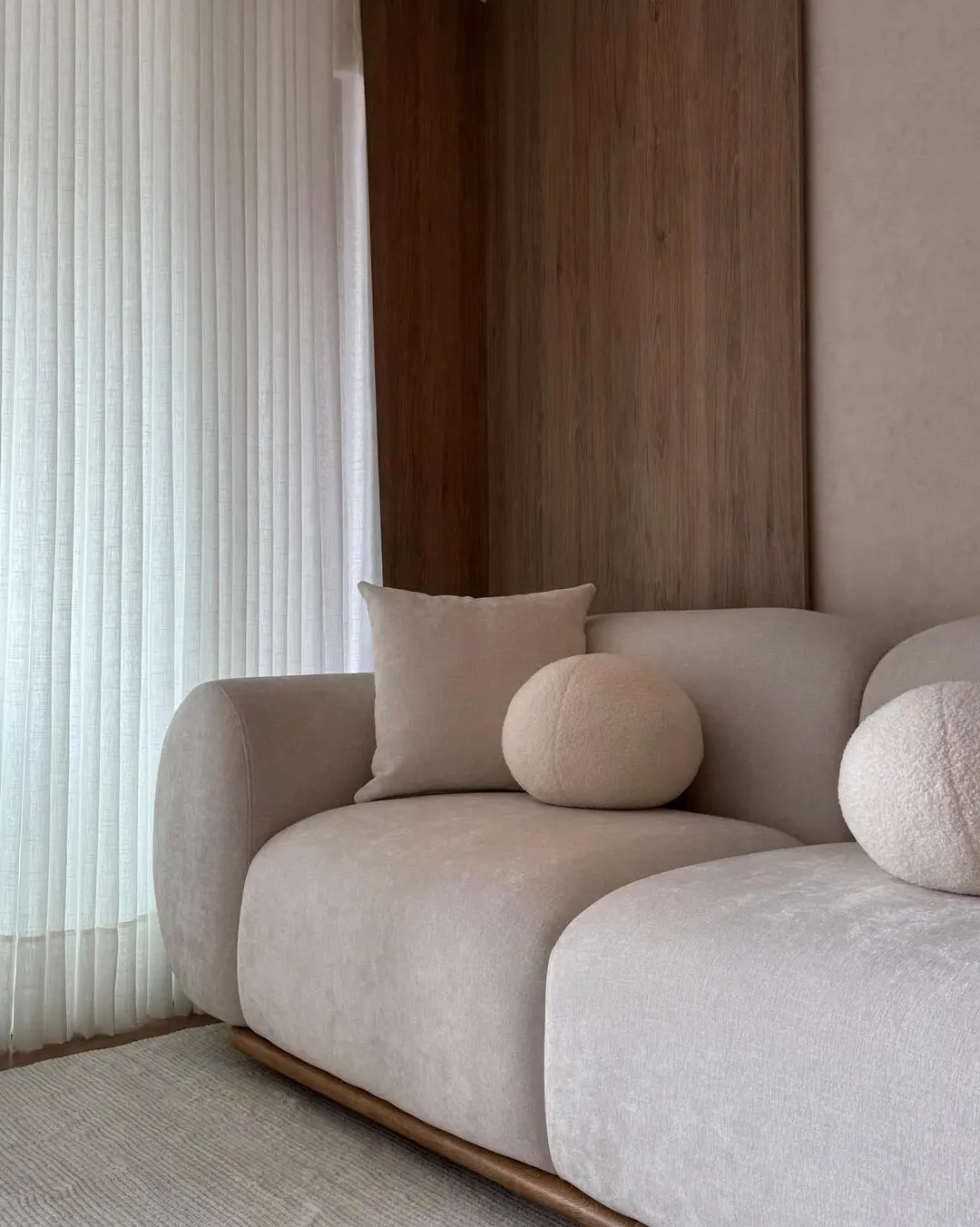 Vista frontal de un sofá de líneas curvas con cojines redondos y cuadrados en tonos beige.